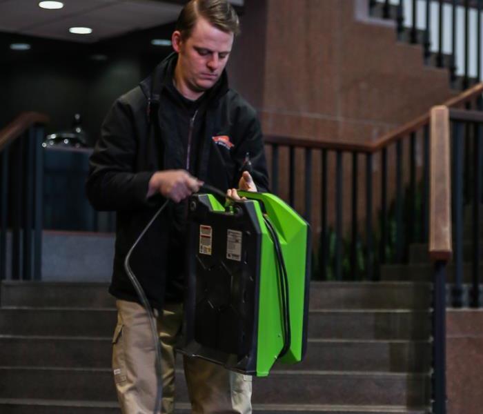 Man carrying SERVPRO equipment with stairs behind him